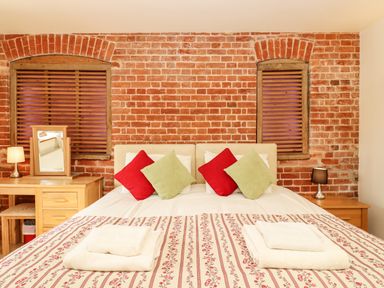 A bedroom with a double bed with red and green cushions and bedside tables with lamps at Poppy Cottage in Little Glemham near Wickham Market