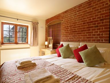 A bedroom with a bed with green and red pillows a window wooden blinds and a wooden dressing table at Poppy Cottage in Little Glemham near Wickham Market