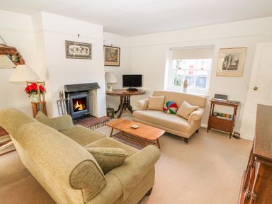 A living room with a green sofa, a beige sofa, a wooden coffee table, a fireplace, a small TV on a round wooden table, and framed pictures on white walls at 28 Oxborough in Oxborough