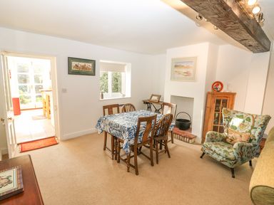 A dining room with a wooden table covered by a blue and white tablecloth surrounded by wooden chairs near a window and an armchair at 28 Oxborough in Oxborough