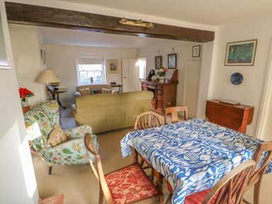 A dining and living room with a wooden dining table with blue and white tablecloth and chairs a green sofa a floral armchair and wooden sideboard at 28 Oxborough in Oxborough