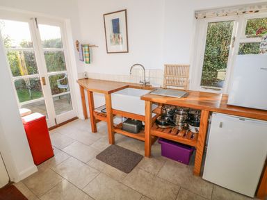 A kitchen with wooden countertops pots and pans under the counter a white sink a small refrigerator a red trash bin and doors leading outside at 28 Oxborough in Oxborough