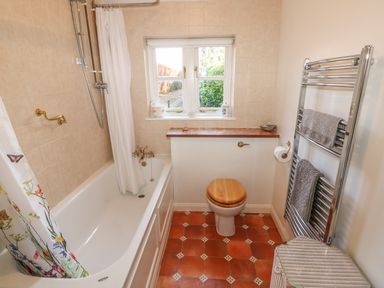 A bathroom with a bathtub with shower curtain a toilet with wooden seat and a towel rack with towels at 28 Oxborough in Oxborough