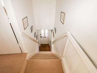 A carpeted staircase with handrails and framed pictures on walls leading to a front door at 28 Oxborough in Oxborough