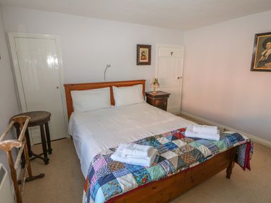 A bedroom with a double bed covered with white linens and a patchwork quilt with towels on it a bedside table with a lamp two closed doors two framed paintings and wooden furniture at 28 Oxborough in Oxborough