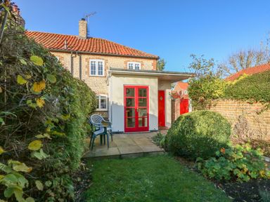 A backyard with a garden, patio with chairs, and a house with red doors and windows at 28 Oxborough in Oxborough