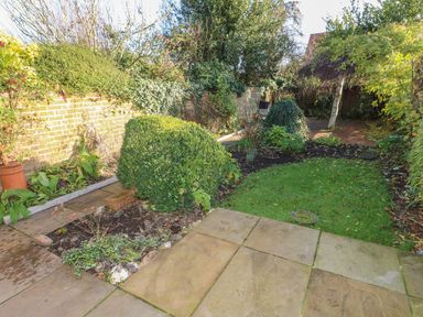 A garden with a paved patio area shrubs grass and trees at 28 Oxborough in Oxborough