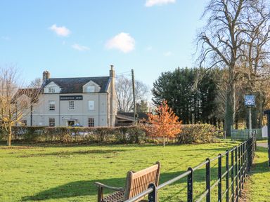 A grassy area with a wooden bench and a building labeled Bedingfeld Arms in Oxborough