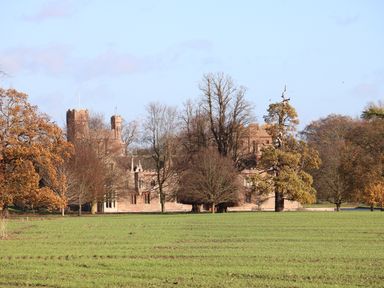 A large brick castle partially hidden by leafless trees and surrounded by grass at 28 Oxborough in Oxborough
