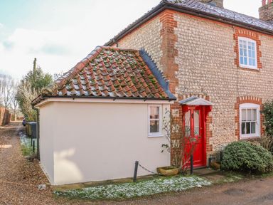 The exterior of a stone and brick house with a red door and tiled roof at 28 Oxborough in Oxborough