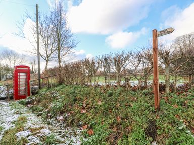 A public footpath signpost next to a hedge and a red telephone box in a grassy area with light snow at 28 Oxborough in Oxborough