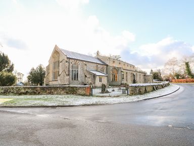 An old stone church with arched windows surrounded by a low stone wall and a gated entrance at 28 Oxborough in Oxborough