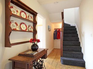 A hallway with a staircase a wooden table with a vase of flowers and a wall-mounted plate shelf at Trysor Y Mor in Borth