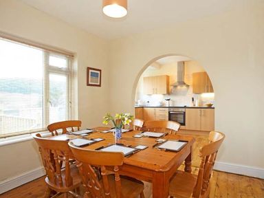 A dining room with a wooden table and chairs next to a window and an archway leading to a kitchen at Trysor Y Mor in Borth