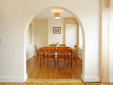 A dining room with a wooden table and six wooden chairs viewed through an archway at Trysor Y Mor in Borth