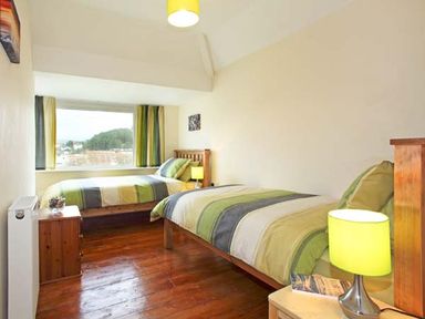A bedroom with two single beds, bedside tables with lamps, and a large window with striped curtains at Trysor Y Mor in Borth