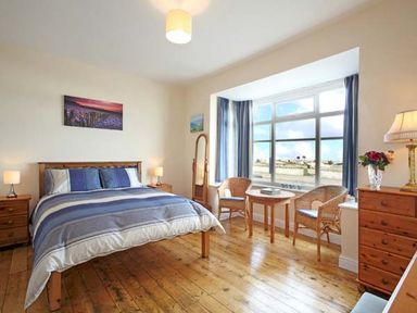 A bedroom with a bed two bedside tables chairs and a table by a large window at Trysor Y Mor in Borth