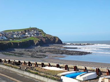 A coastal scene with houses on a hill overlooking a rocky beach and surf boats near the shore at Trysor Y Mor in Borth