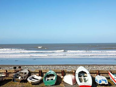 Small boats on shore near the ocean with waves and clear sky at Trysor Y Mor in Borth