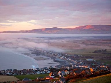 Coastal town with houses along the shore and fog over the land near mountains at Trysor Y Mor in Borth