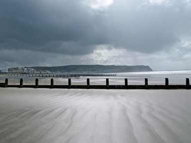A beach with wooden groynes extending into the sea under a cloudy sky at Trysor Y Mor in Borth