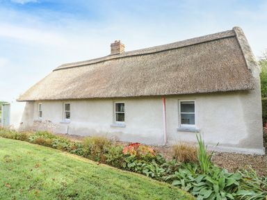 A thatched roof cottage with white walls and small windows surrounded by grass and plants at New Thatch Farm in Scarteen near Knocklong County Limerick