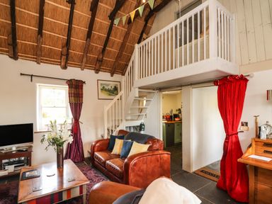 A living room with a leather sofa wooden coffee table and a staircase leading to a loft at New Thatch Farm Scarteen near Knocklong County Limerick