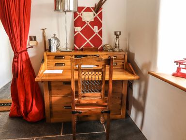 A wooden desk with a wooden chair in front next to a red curtain and a window with a red scale on the windowsill at New Thatch Farm Scarteen near Knocklong County Limerick