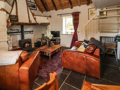 A living room with a wood burning stove two leather sofas a wooden coffee table and a staircase at New Thatch Farm Scarteen near Knocklong County Limerick