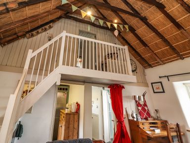 An interior space with a wooden loft and staircase a red curtain a wooden desk and chair and a thatched ceiling at New Thatch Farm Scarteen near Knocklong County Limerick