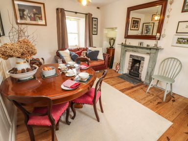 A dining room with a round wooden table set with cups plates and napkins a brown sofa with cushions and a teddy bear a fireplace with a large mirror above it and wooden chairs at New Thatch Farm Scarteen near Knocklong County Limerick