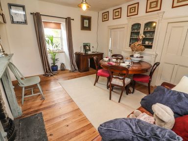 A dining room with a round table set for four chairs a cabinet with glassware a window with curtains and a wooden floor at New Thatch Farm Scarteen near Knocklong County Limerick