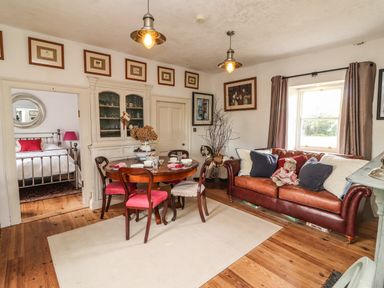 A dining room with a round wooden table and chairs next to a brown leather sofa and a window at New Thatch Farm Scarteen near Knocklong County Limerick
