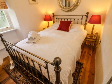 A bedroom with a metal bed frame white bedding red pillow red lamps on bedside tables and wooden floor at New Thatch Farm Scarteen near Knocklong County Limerick