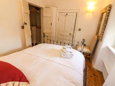 A bedroom with a metal bed frame white bed linens folded towels a wooden floor an open closet a chair a mirror and a door at New Thatch Farm in Scarteen near Knocklong County Limerick