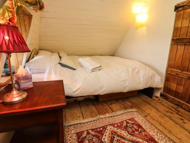 A bedroom with a bed pillows bedside table lamp wooden floor and patterned rug at New Thatch Farm Scarteen near Knocklong County Limerick