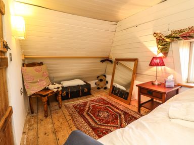 A bedroom corner with a wooden chair and cushion a red patterned rug a mirror a teddy bear a nightstand with a red lamp and a window at New Thatch Farm Scarteen near Knocklong County Limerick