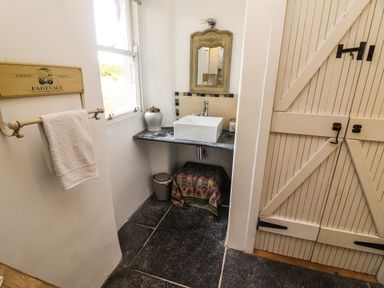 A bathroom with a wall-mounted sink and mirror a towel on a rack and a wooden door at New Thatch Farm Scarteen near Knocklong County Limerick