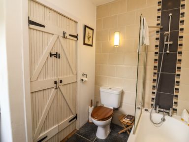 A bathroom with a wooden toilet seat a bathtub with a shower and a rustic wooden door at New Thatch Farm Scarteen near Knocklong County Limerick