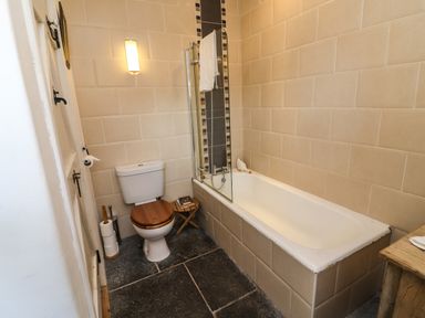 A bathroom with a toilet with wooden lid and a bathtub with a glass shower screen at New Thatch Farm in Scarteen near Knocklong County Limerick