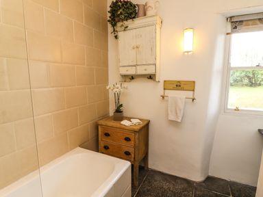 A bathroom with a bathtub wooden cabinet white wall-mounted cupboard and a window at New Thatch Farm Scarteen near Knocklong County Limerick