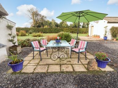 An outdoor patio with a glass table and four chairs with cushions and a large green umbrella at New Thatch Farm Scarteen near Knocklong County Limerick