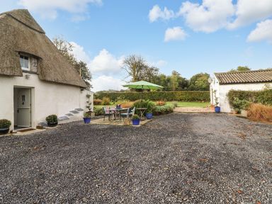 A gravel courtyard with a thatched roof building and outdoor seating with umbrella at New Thatch Farm Scarteen near Knocklong County Limerick