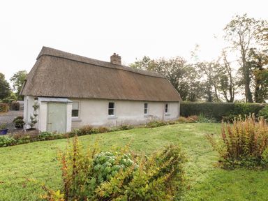 A thatched cottage with white walls and three windows surrounded by a green garden at New Thatch Farm Scarteen near Knocklong County Limerick