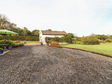 A gravel driveway with a small white building surrounded by plants and a green lawn at New Thatch Farm Scarteen near Knocklong County Limerick