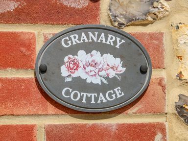 An oval sign reading Granary Cottage with flowers on a brick and stone wall at The Granary Cottage in Gayton near King's Lynn