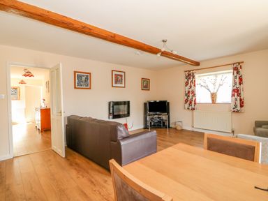 A living room with brown leather sofas a wooden dining table a television and floral curtains at The Granary Cottage in Gayton near Kings Lynn
