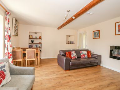 A living room with a brown leather sofa, armchair, dining table with chairs, wooden floor and bookshelves at The Granary Cottage in Gayton near King's Lynn