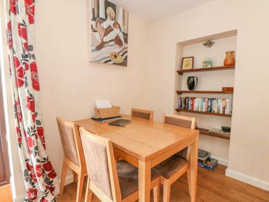 A dining area with a wooden table and four chairs next to shelves with books and decorative items at The Granary Cottage in Gayton near Kings Lynn