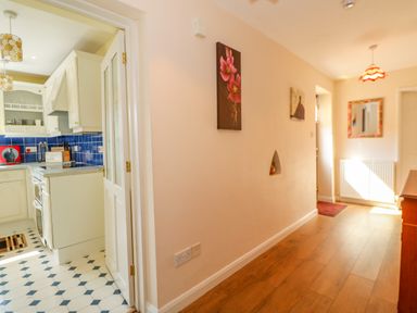 A hallway with wooden flooring and wall decorations leading to a kitchen with white cabinets and blue backsplash at The Granary Cottage in Gayton near King's Lynn